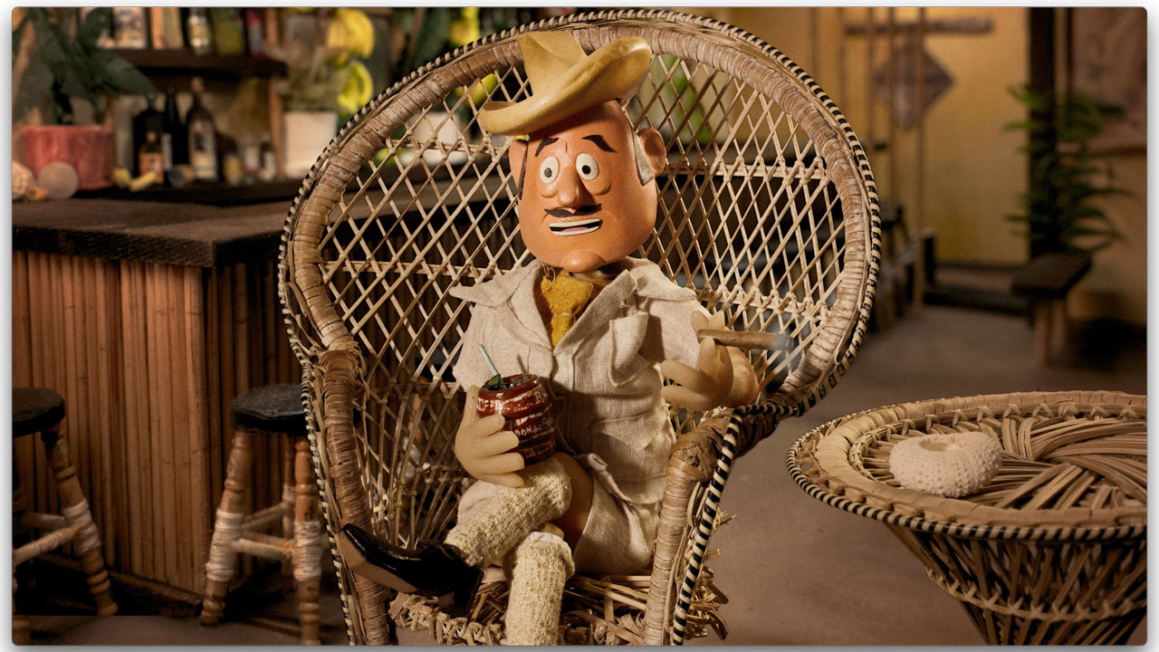 Promotional still from 'The Donn of Tiki' documentary featuring a stop-motion puppet of Don the Beachcomber holding a tiki mug in a tropical bar.